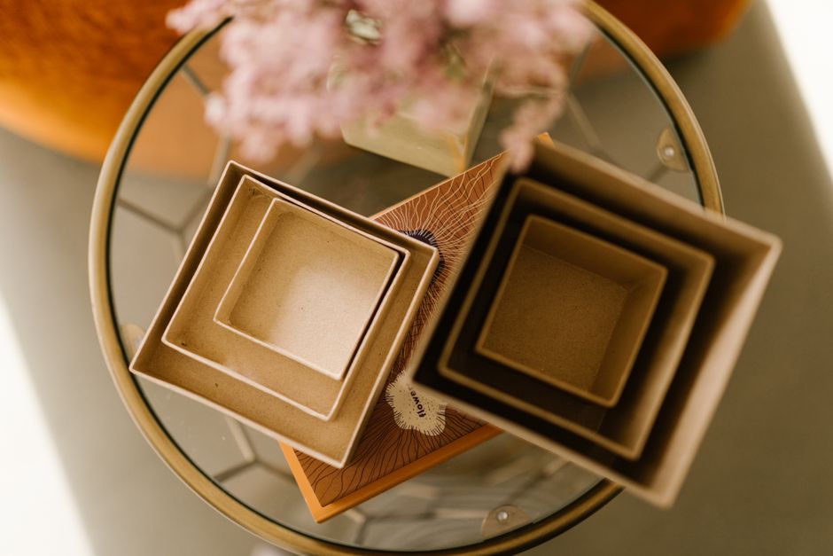 Artistic flat lay of stylish nested cardboard boxes on a glass table with blurred flowers in the background.